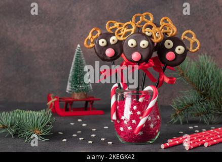 Süße Idee für Weihnachtsleckereien - Cake Pops Santas Rentiere aus Cookies in Schokolade und Cracker auf braunem Hintergrund Stockfoto