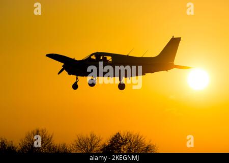 Piper PA-28-161 Cadet landet bei Sonnenuntergang, Wellesbourne Airfield, Warwickshire, Großbritannien (G-FOXA) Stockfoto