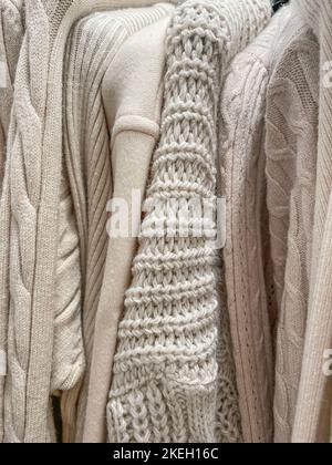 Weiches, gemütliches Strickhintergrundfoto mit verschiedenen Strickpulvern und Pullover in beige-cremefarbener Farbe, die im Stapel in einem Geschäft hängen. Herbst Winter warme Kleidung c Stockfoto