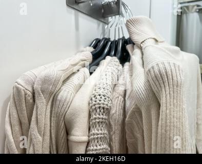 Beige Farbe neu viele Stapel von weichen, gemütlichen Strickpullover mit unterschiedlichem Design hängen an Kleiderbügeln in der Umkleidekammer im Einkaufszentrum. Herbst Winter Saison neu Stockfoto