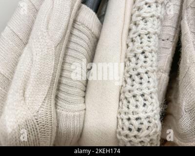 Strickpullover und Pullover in hellbeige Creme auf Kleiderbügeln im Stapelfoto von oben. Warme Bekleidungskollektion für den Herbst Winter. Beige Mode Stockfoto