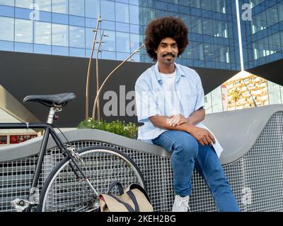 Junger afroamerikanischer Mann mit Afro-Haaren in einem Finanzviertel mit einem Fahrrad. Junger Unternehmer Stockfoto