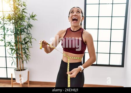 Junge hispanische Frau in Sportkleidung mit Maßband im Sportzentrum wütend und verrückt schreiend frustriert und wütend, schreiend mit Wut schauend Stockfoto