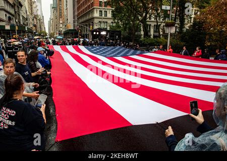 New York, Vereinigte Staaten von Amerika. 11. November 2022. US-Matrosen, die dem amphibischen Transportschiff USS Arlington der San Antonio-Klasse zugewiesen wurden, und Mitglieder der II Marine Expeditionary Force schließen sich Zivilisten an, um während der New York City Veterans Day Parade am 11. November 2022 in New York City, NY, eine riesige amerikanische Flagge zu entrollen. Quelle: MCS John Bellino/US Navy/Alamy Live News Stockfoto