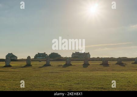 Ausrichtung von Menhir Steinen während der goldenen Stunde auf grüner Wiese und Sonne am Himmel, Camaret-sur-Mer, Bretagne, Frankreich Stockfoto