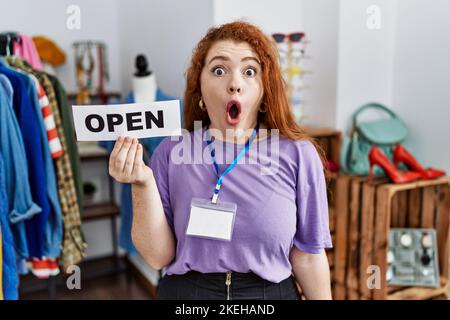 Junge Rotschopf-Frau mit Banner mit offenem Text im Einzelhandel verängstigt und erstaunt mit offenem Mund für Überraschung, Unglauben Gesicht Stockfoto