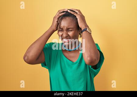 Afrikanische Frau mit Dreadlocks stehen über gelben Hintergrund leiden unter Kopfschmerzen verzweifelt und gestresst, weil Schmerzen und Migräne. Hände auf dem Kopf. Stockfoto