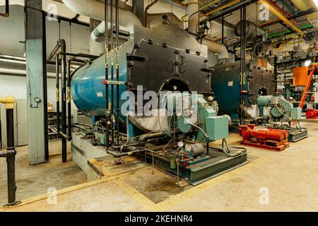 Das Innere eines alten und gut genutzten Kesselraums mit zwei großen Kesseln, vielen Rohren, Ventilen und anderen Geräten. Stockfoto