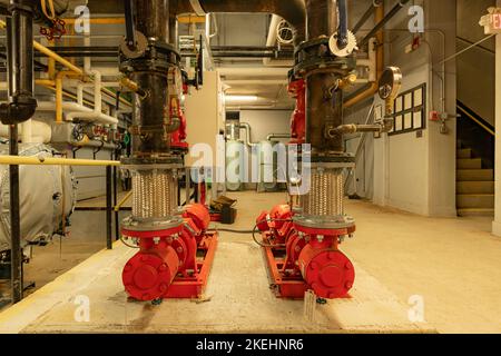 Das Innere eines alten und gut genutzten Kesselraums mit zwei großen mechanischen Pumpen, Rohren, Ventilen und anderen Anlagen. Stockfoto