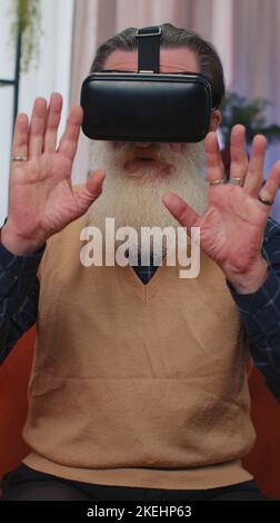 Senior alter Großvater mit Virtual Reality futuristische Technologie VR-App Headset Helm Simulation 3D Videospiel spielen, Film-Film in der modernen Wohnung zu Hause zu sehen. Mann in Schutzbrille. Vertikale Ansicht Stockfoto