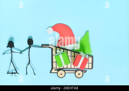 Happy Christmas Shopping-Konzept. Paar Stick Figur schieben einen Warenkorb mit Weihnachtsgeschenken flach Lay Komposition. Stockfoto