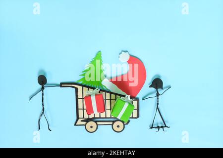 Happy Christmas Shopping-Konzept. Paar Stick Figur schieben einen Warenkorb mit Weihnachtsgeschenken flach Lay Komposition. Stockfoto