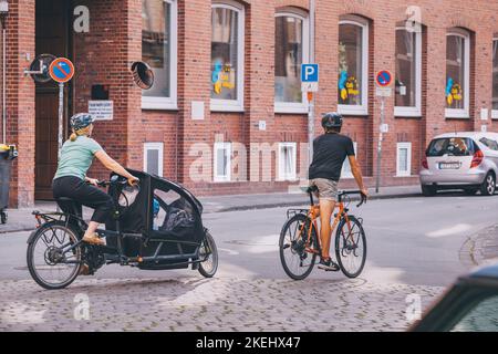 25. Juli 2022, Münster, Deutschland: Eine Sportfamilie - Vater und Mutter mit Kind fahren mit dem Fahrrad durch die Straßen einer alten europäischen Stadt Stockfoto