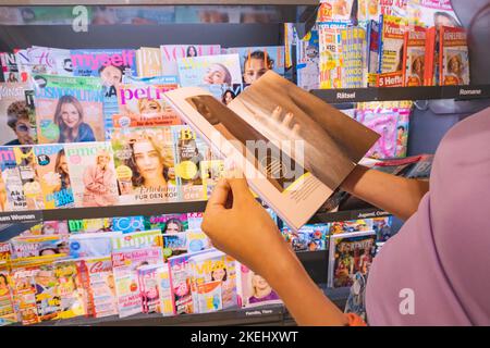 25. Juli 2022, Münster, Deutschland: Kundin liest Modemagazine, Boulevardzeitungen und Zeitschriften mit Anzeigen an der Ladentheke im deutschen lan Stockfoto