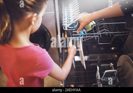 Das scheint sauber zu sein. Über die Schulter eines unerkennbaren kleinen Mädchens, das zu Hause Geschirr in einer Spülmaschine verpackt. Stockfoto