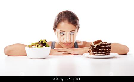 Du weißt, was ich will. Studioaufnahme einer attraktiven jungen Frau, die sich zwischen gesunden und ungesunden Lebensmitteln entscheidet. Stockfoto