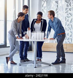 Ihre gleichgesinnten Kollegen. Eine Gruppe von Kollegen, die in einem Büro zusammen an einem Laptop arbeiten. Stockfoto