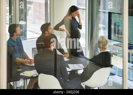 Arbeiten und Schwangerschaft sind wie zwei Jobs. Eine Schwangere Geschäftsfrau, die sich während eines Treffens in Unwohlsein verquem fühlt. Stockfoto