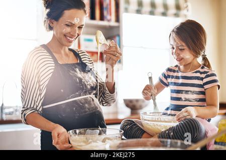 Backen ist eine Teamarbeit, die sie gerne teilen. Ein kleines Mädchen, das Spaß hat, während es mit ihrer Mutter in der Küche backt. Stockfoto