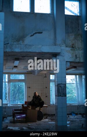 Post-Apokalypse. Eine junge Frau sitzt und raucht in einem verlassenen Gebäude. Konzept eines Mannes, der in einer post-apokalyptischen Welt auf der Suche nach Nahrung wandert. Stockfoto
