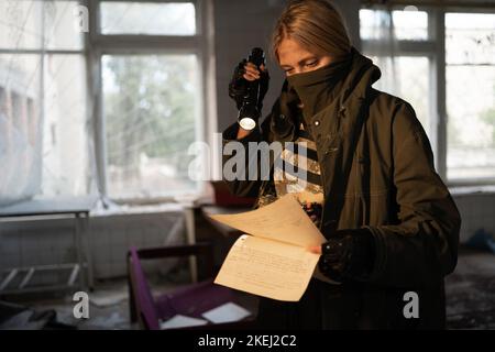 Nukleare Post-Apokalypse Leben nach Weltuntergang Konzept. Schmutzige weibliche Überlebende in Maskenlesung in verlassenen Gebäude drinnen Stockfoto