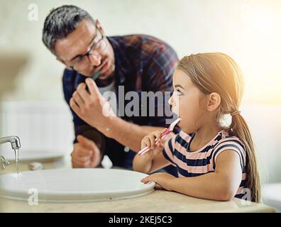 Stellen Sie sicher, dass Sie richtig putzen ... ein schöner reifer Mann und seine Tochter putzen ihre Zähne im Badezimmer. Stockfoto