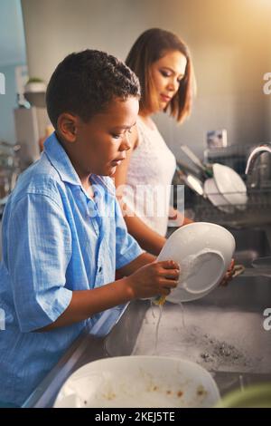 HES gibt Mama eine helfende Hand. Mutter und Sohn waschen gemeinsam Geschirr. Stockfoto