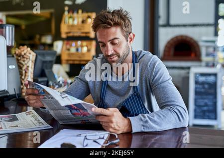 Ein hübscher junger Mann, der in einem Café sitzt und eine Zeitung liest. Stockfoto