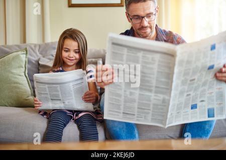 Es ist gut, neugierig zu sein. Ein Vater und eine Tochter lesen die Zeitung. Stockfoto