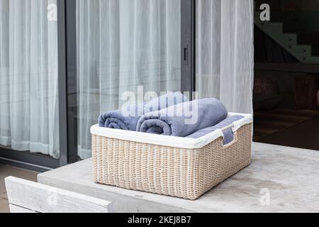 Blaue Badetücher im Korbkorb auf einem Betontisch im sonnigen Garten Stockfoto
