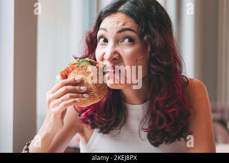 Ein Mädchen schnüffelt einen verwöhnten Burger. Fast-Food-Diät und Lebensmittelvergiftung Konzept Stockfoto