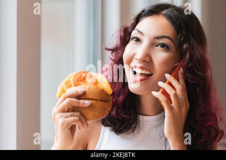 Eine Frau isst in einem Fast-Food-Café einen Hamburger und telefoniert mit einem Freund Stockfoto