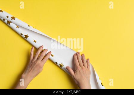 Frauenhänden öffnen Geschenkpapier mit Sternen für Geschenke auf gelbem Hintergrund Stockfoto