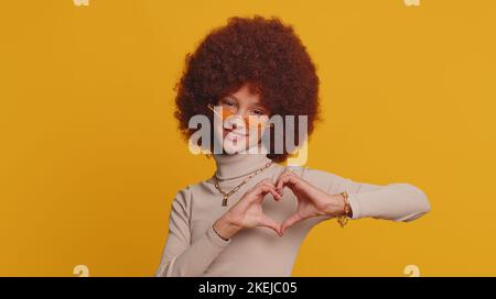 Ich liebe dich. Lächelnd junger Teenager Kind Mädchen Kind macht Herz Geste zeigt Liebe Zeichen drückt gute Gefühle und Sympathie. Kleine lustige Kinder isoliert allein auf Studio gelben Hintergrund Stockfoto