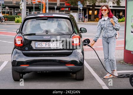 26. Juli 2022, Münster, Deutschland: Ein Mädchen berechnet ihr Smart-Auto für zwei Personen auf einem kostenlosen Parkplatz für Öko-Elektroautos in der Stadt Stockfoto