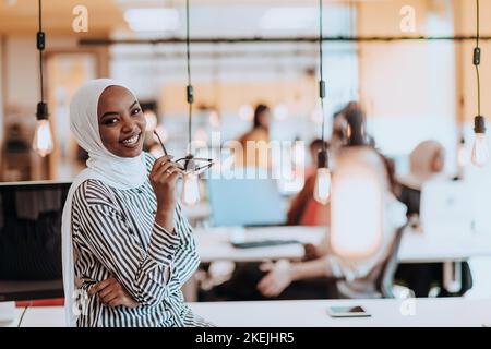 Trait einer schwarzen (afroamerikanischen) weiblichen muslimin, die in einem modernen Geschäftsbüro steht, während sie einen Hijab trägt. Stockfoto