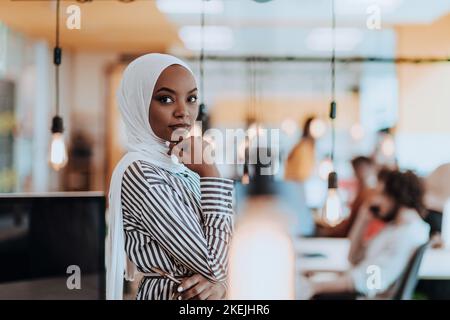 Trait einer schwarzen (afroamerikanischen) weiblichen muslimin, die in einem modernen Geschäftsbüro steht, während sie einen Hijab trägt. Stockfoto