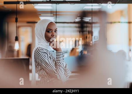 Protrait einer schwarzen afroamerikanischen muslimin, die in einem modernen Geschäftsbüro steht, während sie einen Hijab trägt. Stockfoto