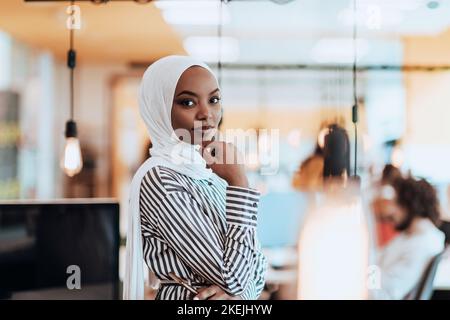 Trait einer schwarzen (afroamerikanischen) weiblichen muslimin, die in einem modernen Geschäftsbüro steht, während sie einen Hijab trägt. Stockfoto