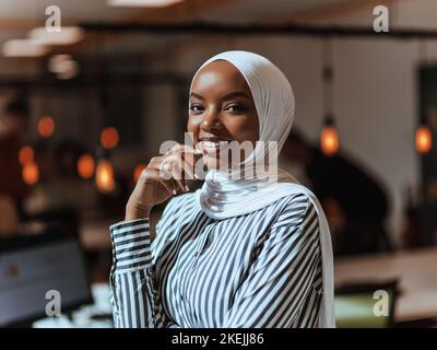 Trait einer schwarzen (afroamerikanischen) weiblichen muslimin, die in einem modernen Geschäftsbüro steht, während sie einen Hijab trägt. Stockfoto