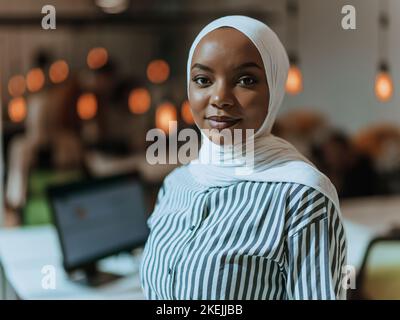Trait einer schwarzen (afroamerikanischen) weiblichen muslimin, die in einem modernen Geschäftsbüro steht, während sie einen Hijab trägt. Stockfoto