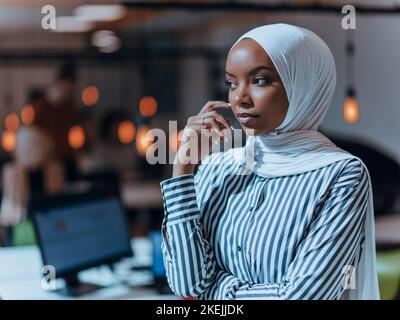 Trait einer schwarzen (afroamerikanischen) weiblichen muslimin, die in einem modernen Geschäftsbüro steht, während sie einen Hijab trägt. Stockfoto