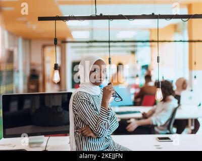 Trait einer schwarzen (afroamerikanischen) weiblichen muslimin, die in einem modernen Geschäftsbüro steht, während sie einen Hijab trägt. Stockfoto
