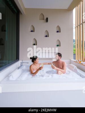 Ein Paar trinkt Champagner in einem Whirlpool während der Flitterwochen, asiatische Thai-Frauen und kaukasische Männer in einem Whirlpool im Freien Stockfoto