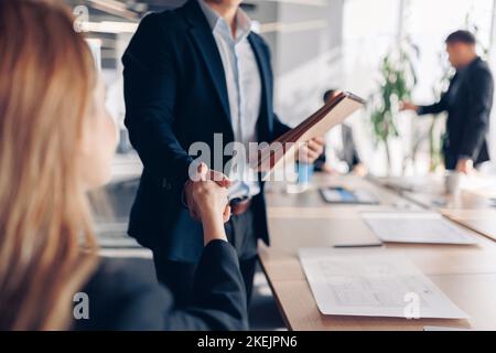 Nahaufnahme von zwei Kollegen, die sich die Hände schütteln, während sie vor dem Meeting im Büro sitzen Stockfoto