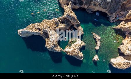 Luftdrohnenaufnahme von Kajaks und Booten, die um die magischen Kalksteinfelsen von Ponta da Piedade vorbeifahren. Erkundung von Höhlen und Tunneln der Algarve von Lagos Portugal Stockfoto