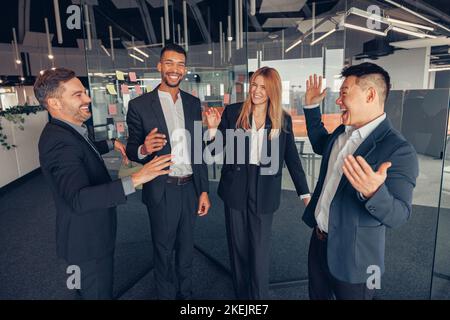 Eine Gruppe lächelnder, multitnischer Kollegen, die in der Pause miteinander sprechen, während sie im Büro stehen Stockfoto