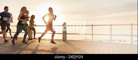 Fit Menschen laufen ein Marathon-Rennen entlang einer Promenade am Meer. Läufer und Läuferinnen treten bei einem Lauf an, fördern aber gleichzeitig einen gesunden Lebensstil und ein Stockfoto