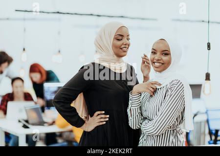 Porträt zweier afroamerikanischer Geschäftsfrauen, die miteinander sprechen, während sie mit ihren Kollegen in einem modernen Geschäftsbüro stehen. Marketing Stockfoto