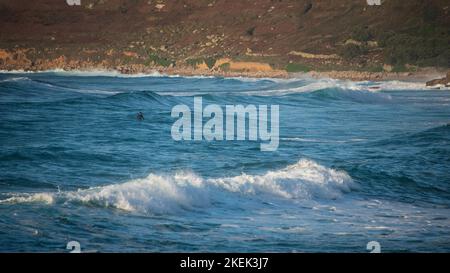 Nicht identifizierte Surfer reiten während des späten Sonnenuntergangs auf den Wellen von Sennen Cove in Cornwall Stockfoto